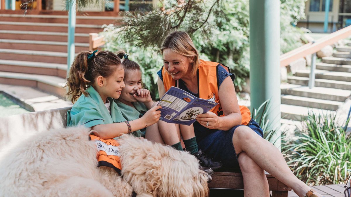 Two young girls reading with a Story Dog volunteer and her dog